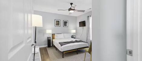 A bedroom with a bed, bedside tables, a ceiling fan, and a TV on the wall.