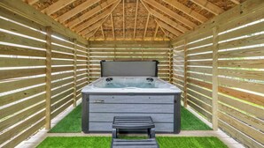Een hottub onder een houten constructie met een lessenaarsdak en een bank ervoor.