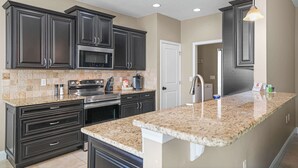 A modern kitchen with dark cabinetry, granite countertops, stainless steel appliances, and recessed ceiling lights. - Beach Haven: 6 Beds, Pet Friendly, 8miles to Beach (Mary Esther)
