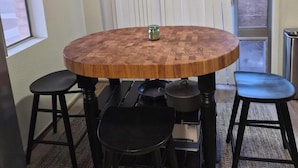 Une table ronde en bois, quatre tabourets noirs, un petit bocal en verre et un pot noir posés sur la table.