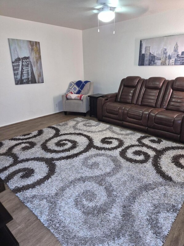 A living room with a brown leather sofa, a patterned rug, and two wall-mounted paintings.