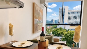 Mesa lista con platos, servilletas y una botella de vino, con vista a un paisaje urbano a través de un ventanal amplio.