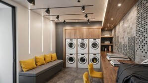 Un moderno cuarto de lavado con lavadora y secadora integradas, un banco con cojines amarillos y una encimera de madera con ropa doblada.