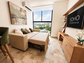 Una sala de estar moderna con sofá, cama abatible, mueble de madera y un gran ventanal con vistas a la ciudad.