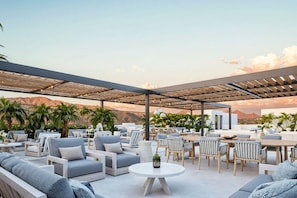Une terrasse extérieure aménagée avec des coins salon, des tables et une vue sur les montagnes.