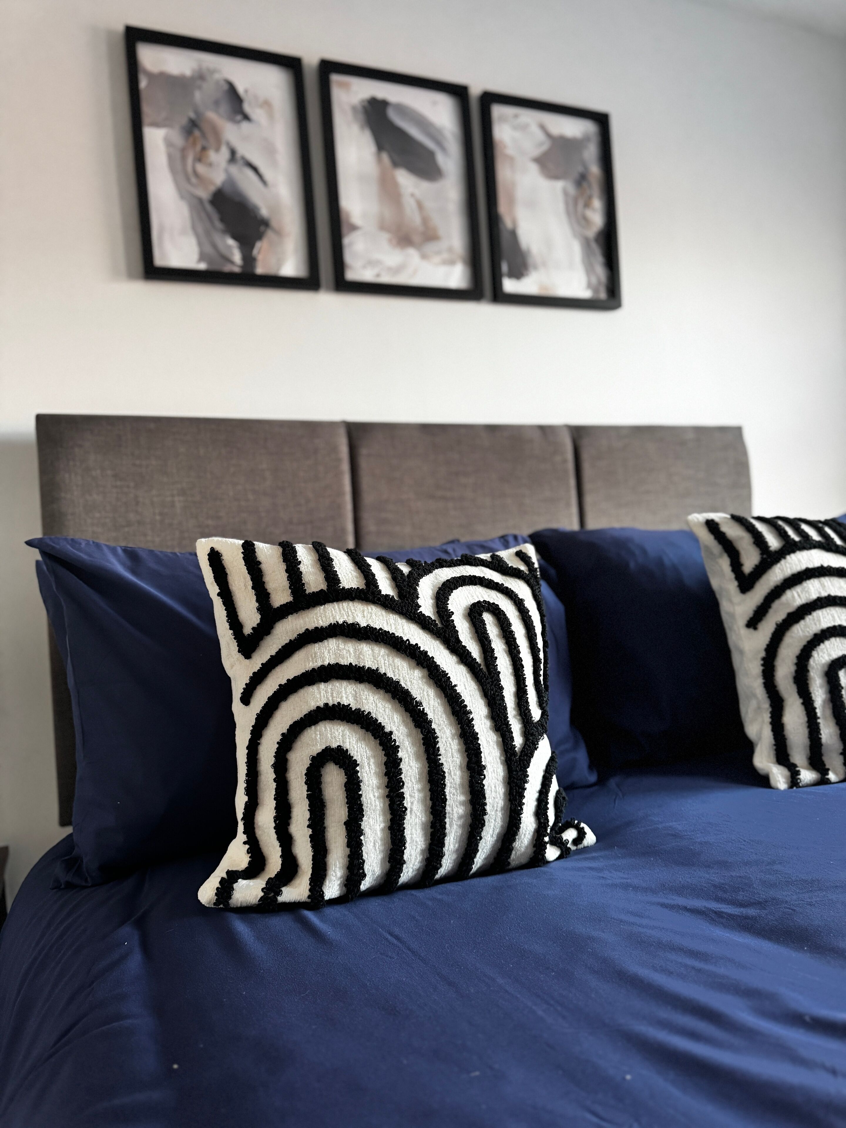 Un lit avec une literie bleu foncé et deux coussins décoratifs à motifs noir et blanc.