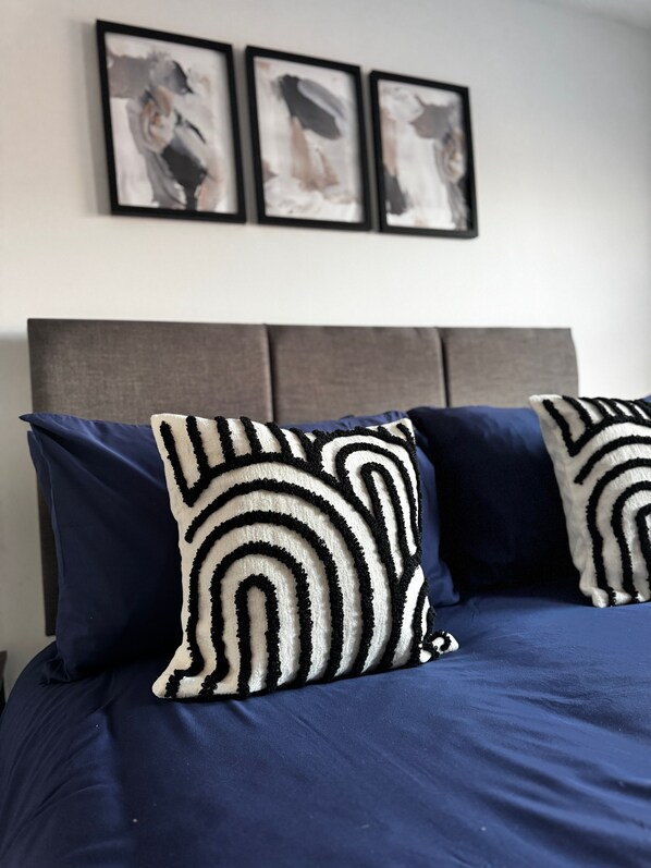 A bed with dark blue bedding and two decorative pillows with a black and white pattern.
