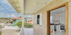 A balcony with a view of neighboring houses, a kitchen with white cabinets and a tiled backsplash, and a wooden door frame. - Bela casa a 250m da Praia Santinho Florianópolis (Florianópolis)