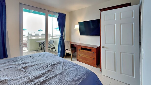 A hotel room with a bed, a desk with a chair, a television, and a sliding door to a balcony with outdoor seating. - Harbour Beach Resort 105 (Daytona Beach)