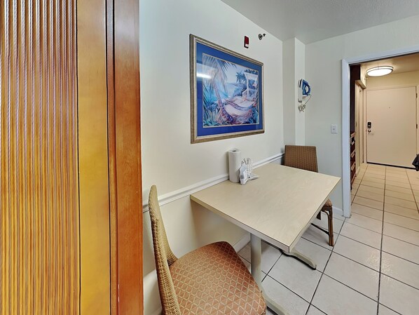 A dining area with a table, chairs, and a framed painting on the wall. - Harbour Beach Resort 205 (Daytona Beach)