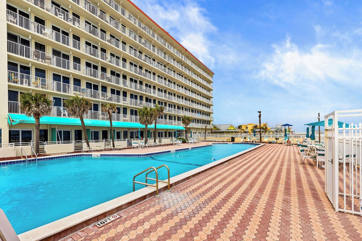 A hotel with a swimming pool, outdoor seating, and a view of the ocean.