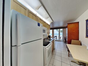 A compact kitchen with a refrigerator, microwave, and stove. It leads to a balcony with a table and chairs, overlooking a scenic view. - Harbour Beach Resort 205 (Daytona Beach)