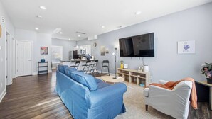 Uma sala de estar moderna com um sofá azul, uma poltrona cinza e uma televisão de tela plana presa na parede.