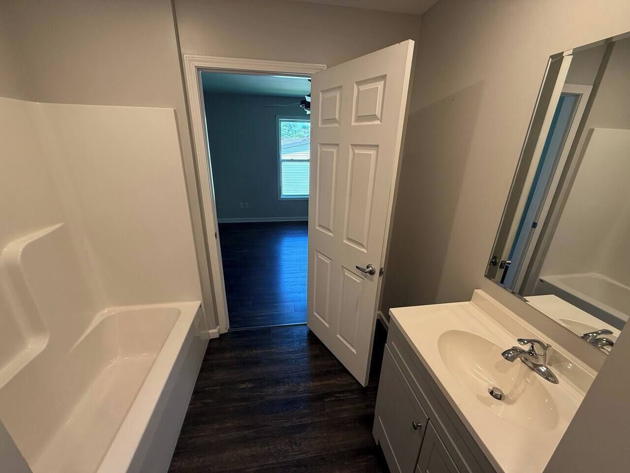 A narrow bathroom with a bathtub, a sink, and a door leading to another room.