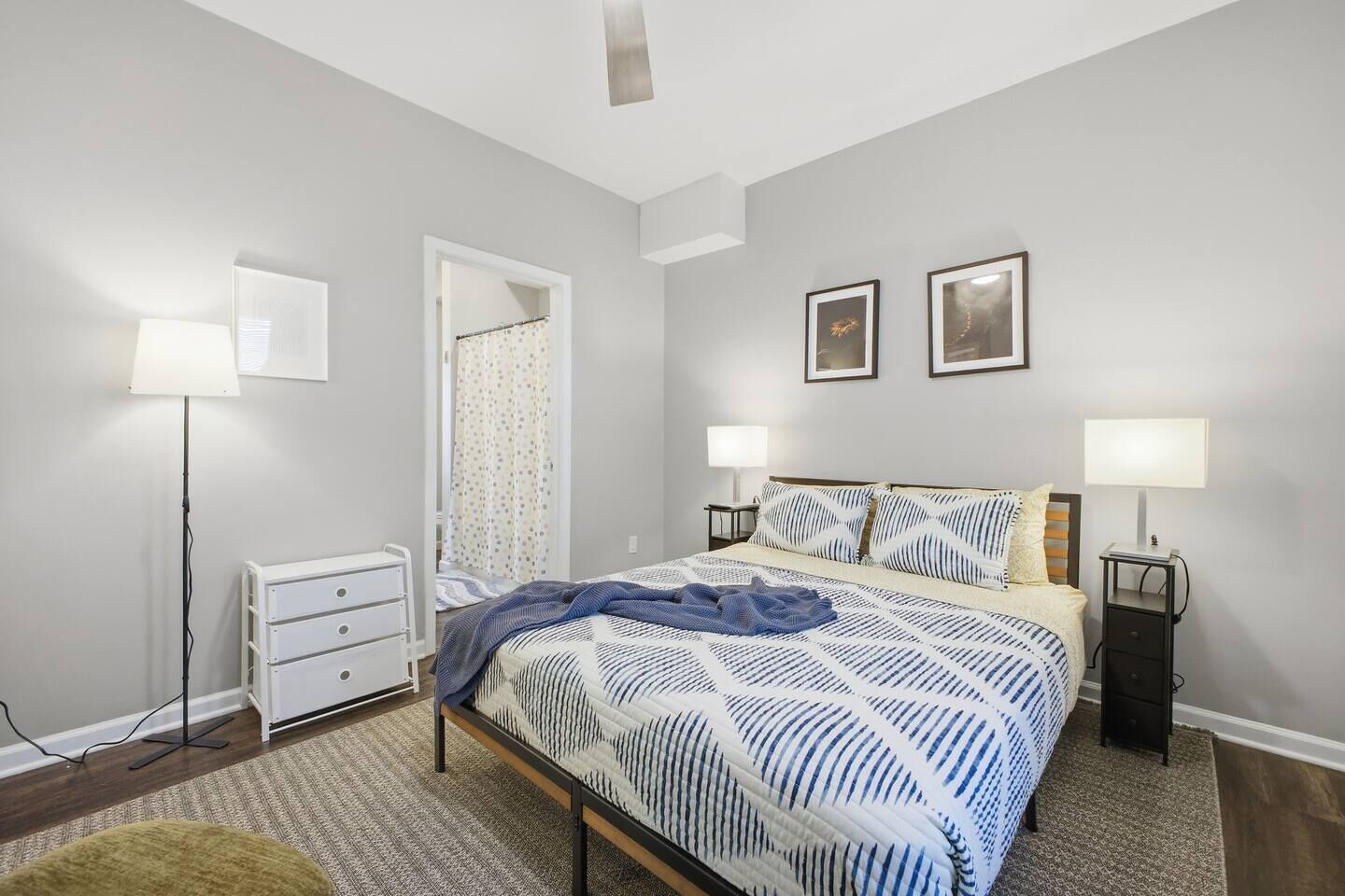 A bedroom with a bed, bedside lamps, a nightstand, a dresser, and a door with a curtain.