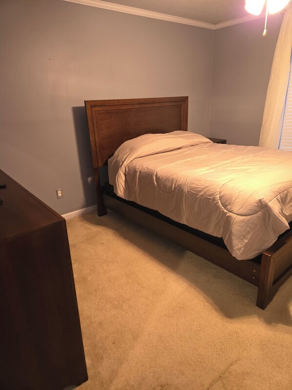A bedroom with a wooden bed frame, beige carpet, and a nightstand.