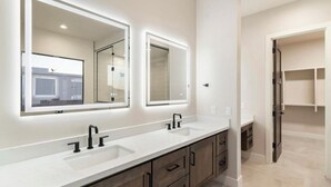 Ein modernes Badezimmer mit zwei Waschbecken, großen Spiegeln und einem begehbaren Kleiderschrank.