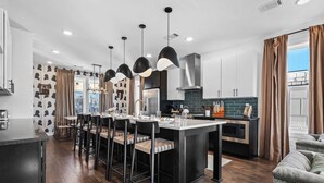 A modern kitchen with a central island, bar stools, pendant lighting, and a dining area with chairs. - City Views | Rooftop Deck | Fire Pit + Grill (Nashville)