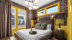 A bedroom with a large bed, a bedside table, a mirror, and a window with curtains. - City Views | Rooftop Deck | Fire Pit + Grill (Nashville)
