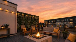 A rooftop terrace with a fire pit, seating, and string lights against a sunset sky. - City Views | Rooftop Deck | Fire Pit + Grill (Nashville)