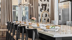 A modern dining area with a long table set for a meal, black chairs, a central island with a sink, and a large refrigerator. - City Views | Rooftop Deck | Fire Pit + Grill (Nashville)