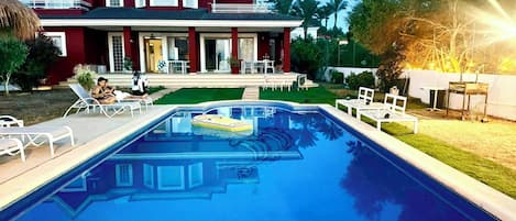 A swimming pool with lounge chairs, a house with a balcony, and a well-maintained lawn.