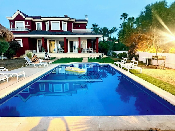 A swimming pool with lounge chairs, a house with a balcony, and a well-maintained lawn. - Red House Rooms (Llucmajor)