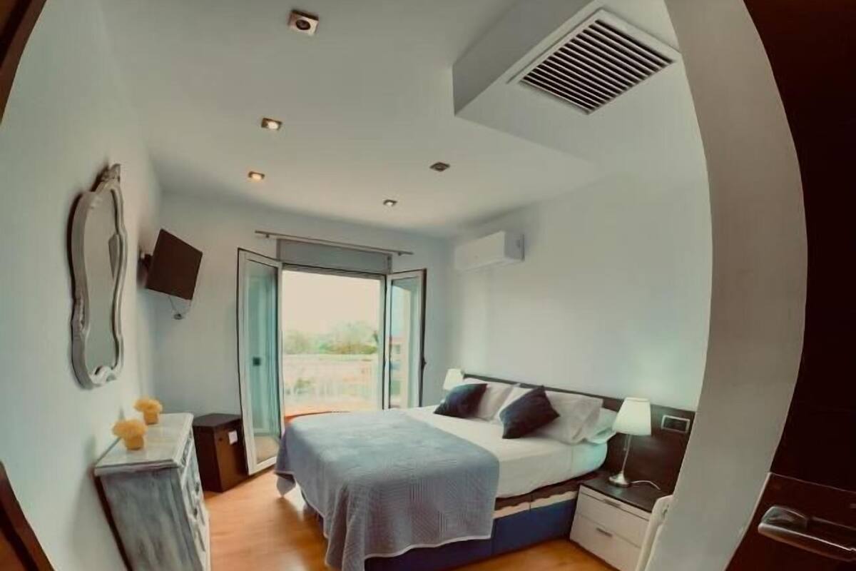 A bedroom with a bed, bedside table, lamp, and a view through a sliding door to the outside.