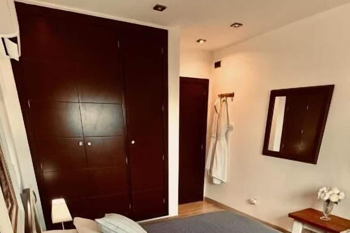 A bedroom with a large bed, a wooden nightstand, a wardrobe, and a small table with a vase.