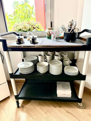 A kitchen cart with utensils, a coffee maker, and a box labeled "4x BERGVATTNET" on a shelf. - Red House Rooms (Llucmajor)