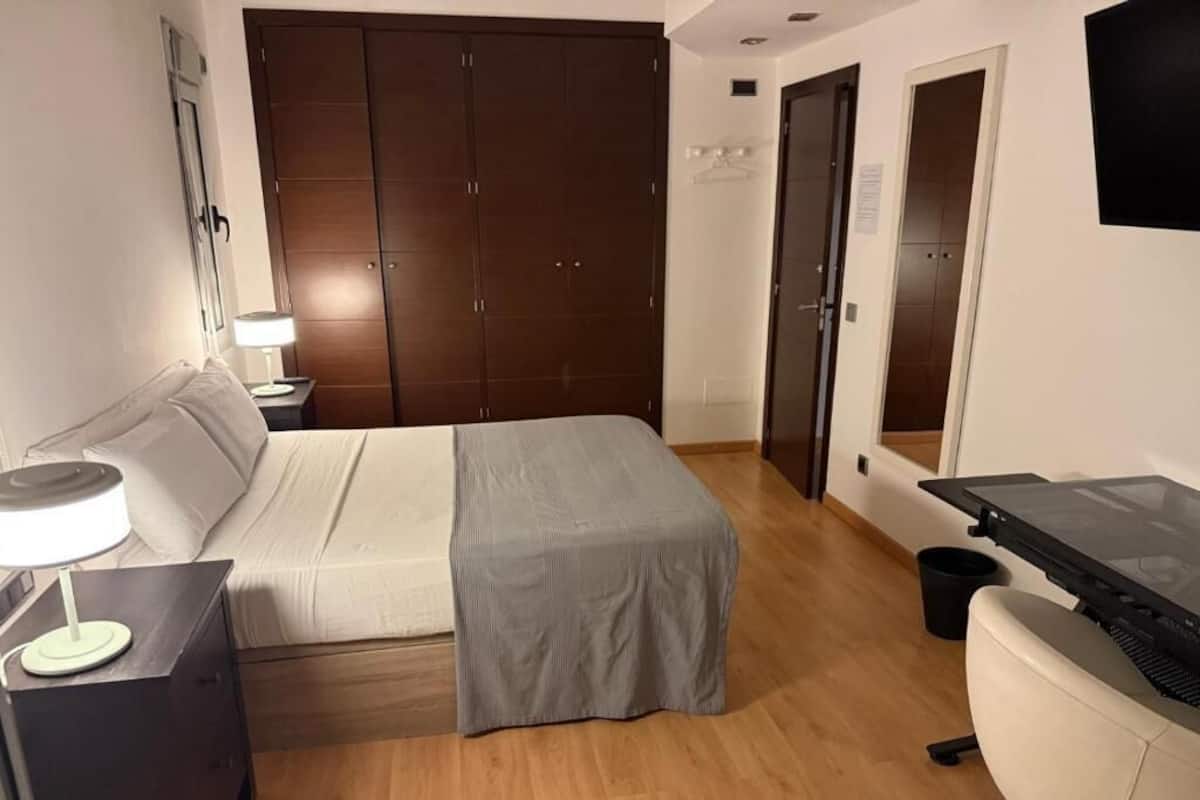 A bedroom with a bed, a desk, a chair, a wardrobe, and a TV.