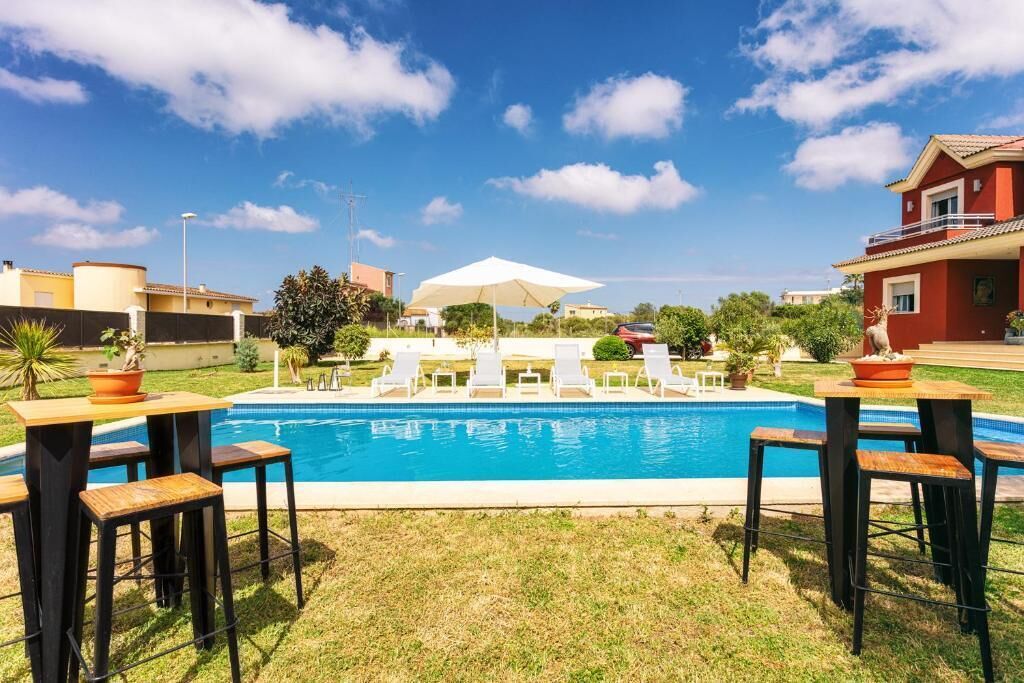 A swimming pool with lounge chairs and a table, surrounded by grass and a few trees.