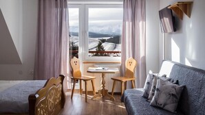 A room with a bed, a sofa, a table with two chairs, and a view of mountains through a window. - Miedzy Owcami Meee (Czorsztyn)