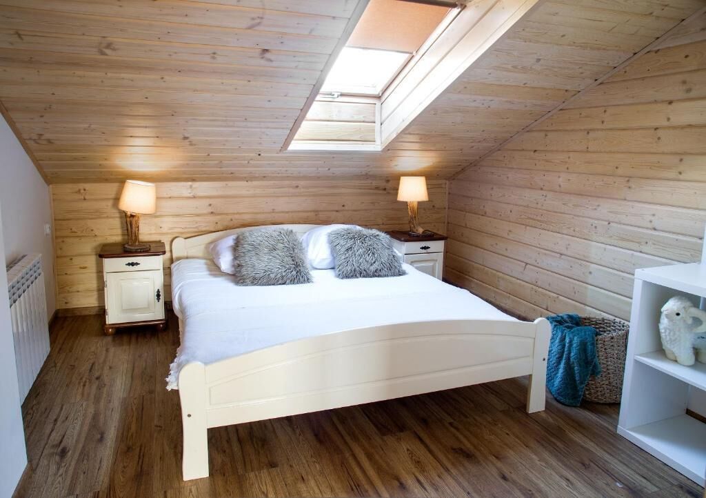 A bedroom with a sloped ceiling, a skylight, a bed with white bedding, two bedside tables with lamps, and a white shelf with a decorative item.