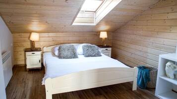 A bedroom with a sloped ceiling, a skylight, a bed with white bedding, two bedside tables with lamps, and a white shelf with a decorative item.