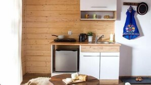 A cozy room with a wooden ceiling, a small kitchen area with a fridge, a table with bread, and a fluffy white dog. - Miedzy Owcami Meee (Czorsztyn)