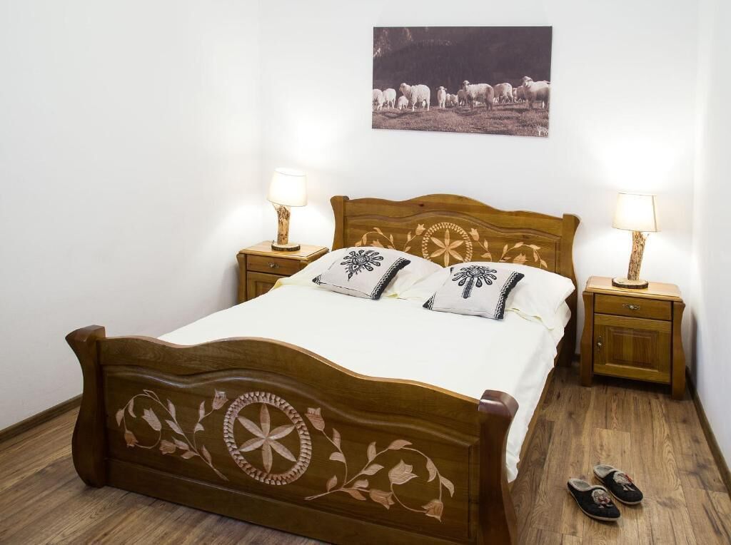 A wooden bed with floral carvings, two bedside tables with lamps, and a framed picture on the wall.