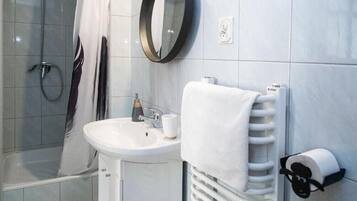 A bathroom with a shower, sink, mirror, towel rack, and toilet paper holder.