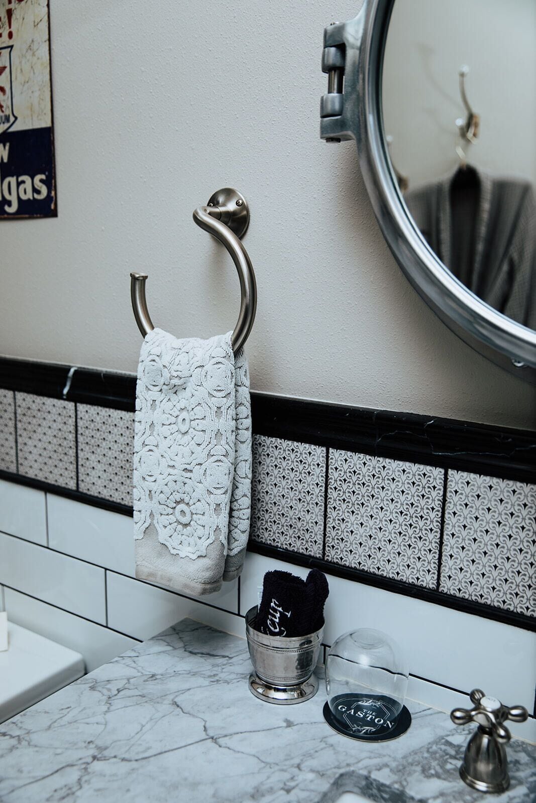 A bathroom with a towel rack, a mirror, a sink with a marble countertop, and a decorative metal object.