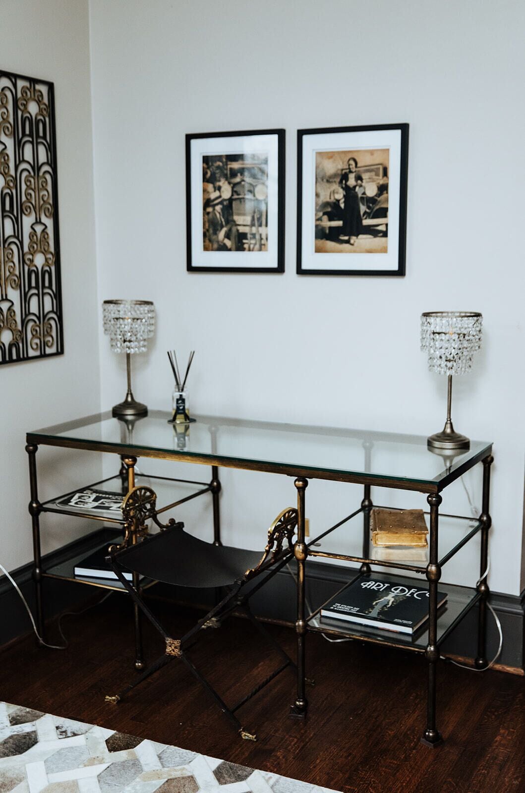 A room with a glass-top table, two black chairs, a decorative metal wall piece, and two framed photographs.