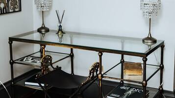 A room with a glass-top table, two black chairs, a decorative metal wall piece, and two framed photographs.