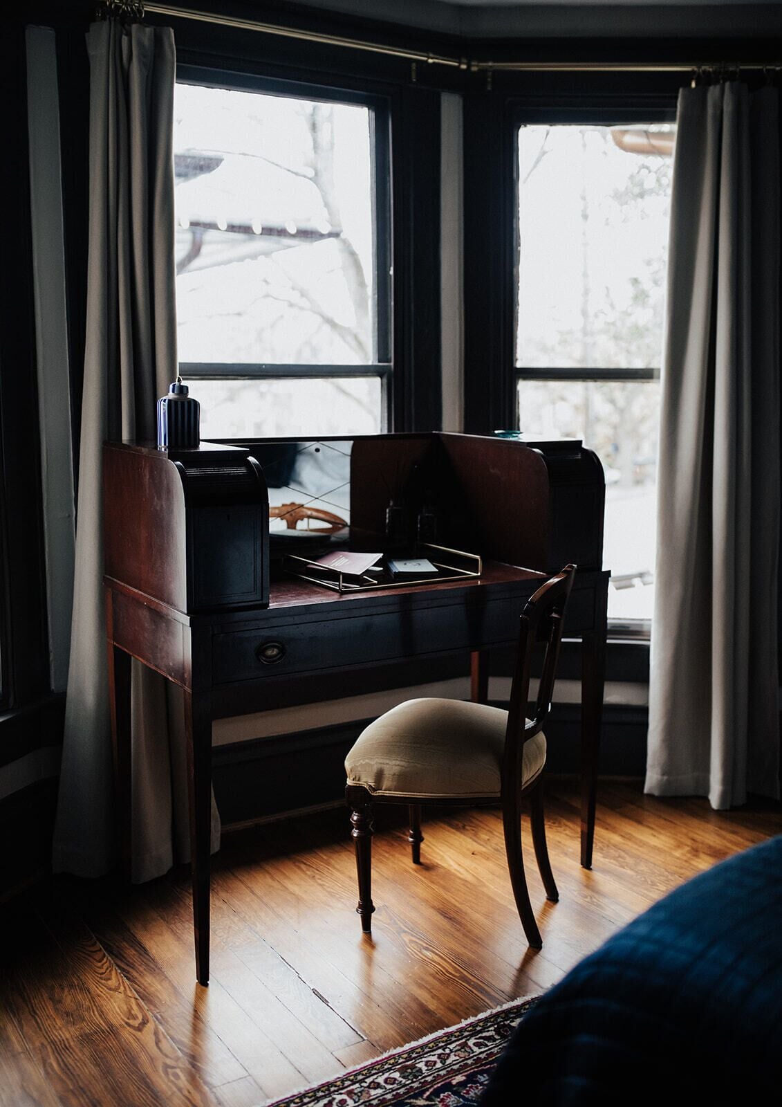 A wooden desk with a chair, a lamp, and a window with curtains.