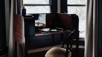 A wooden desk with a chair, a lamp, and a window with curtains.