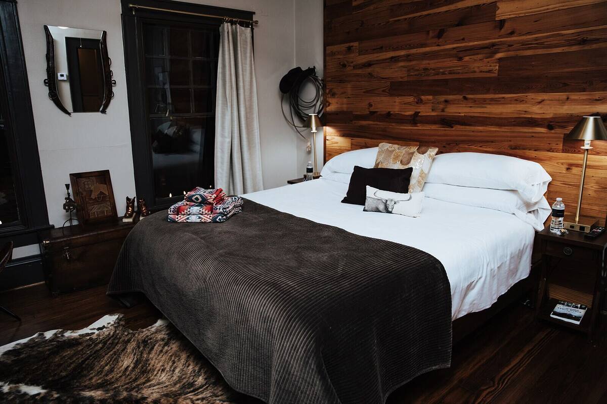 Een slaapkamer met een groot bed, een houten hoofdbord, een nachtkastje met een lamp en een spiegel aan de muur.