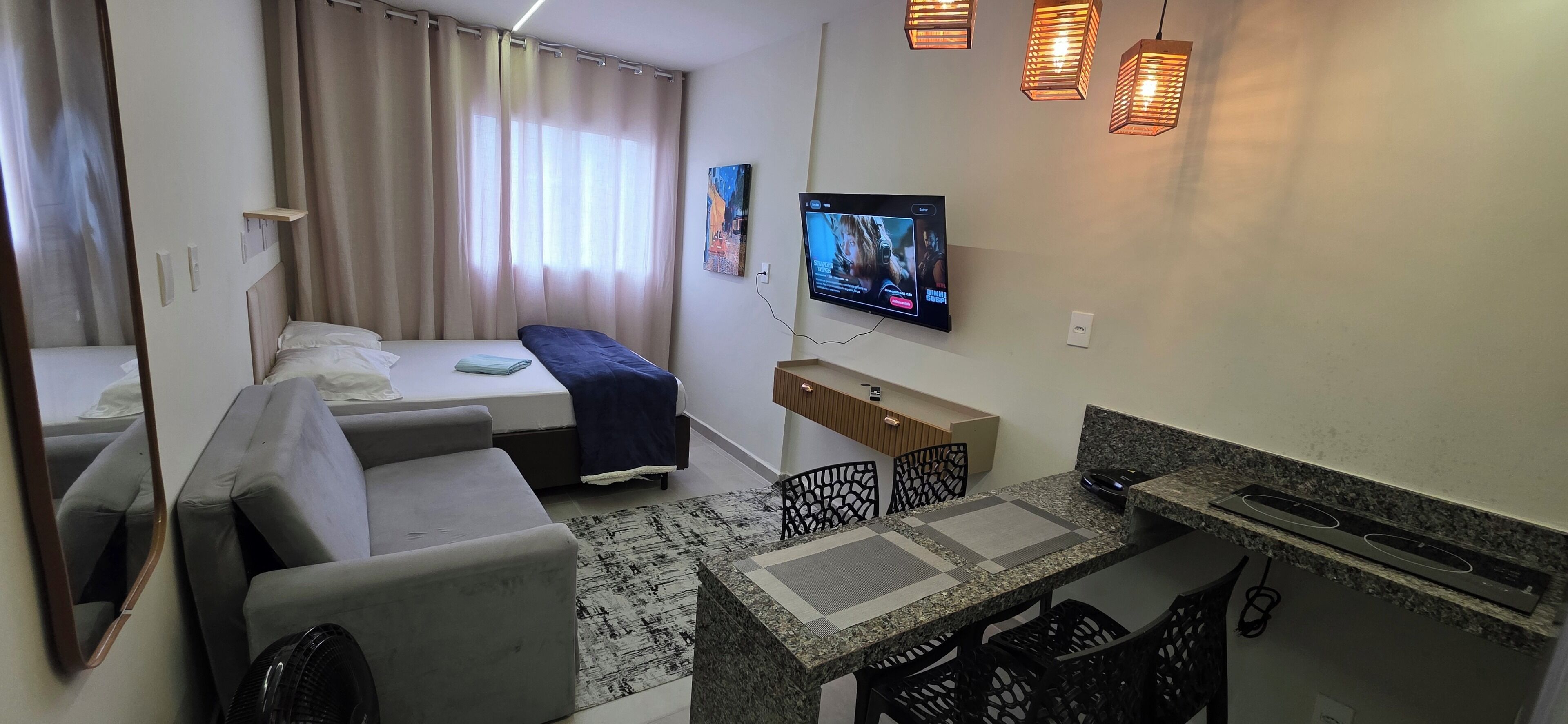 Habitació d'hotel moderna amb sofà, llit, televisió, taula petita i zona de cuina.