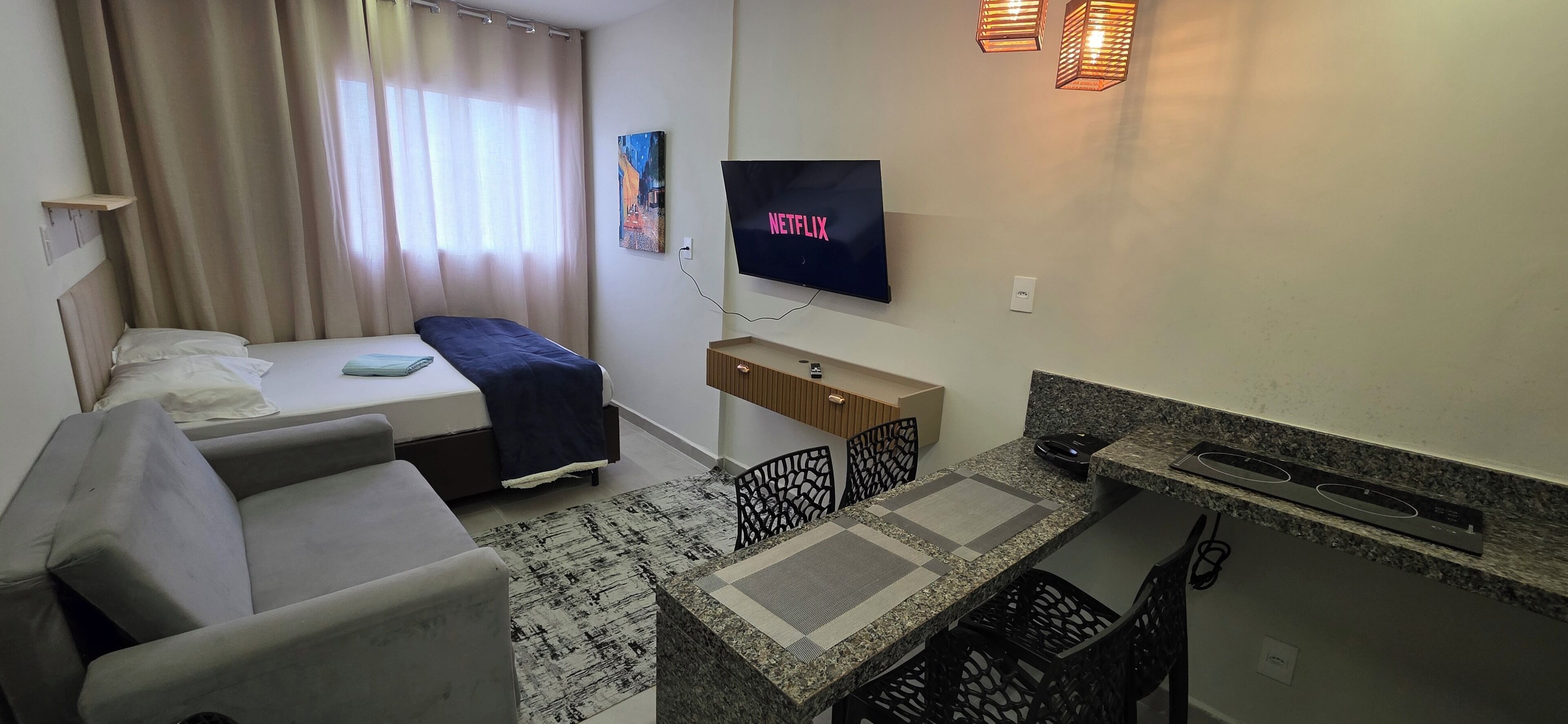 Een hotelkamer met een bed, een bank, een aan de muur bevestigde televisie, een kleine tafel en een kitchenette.