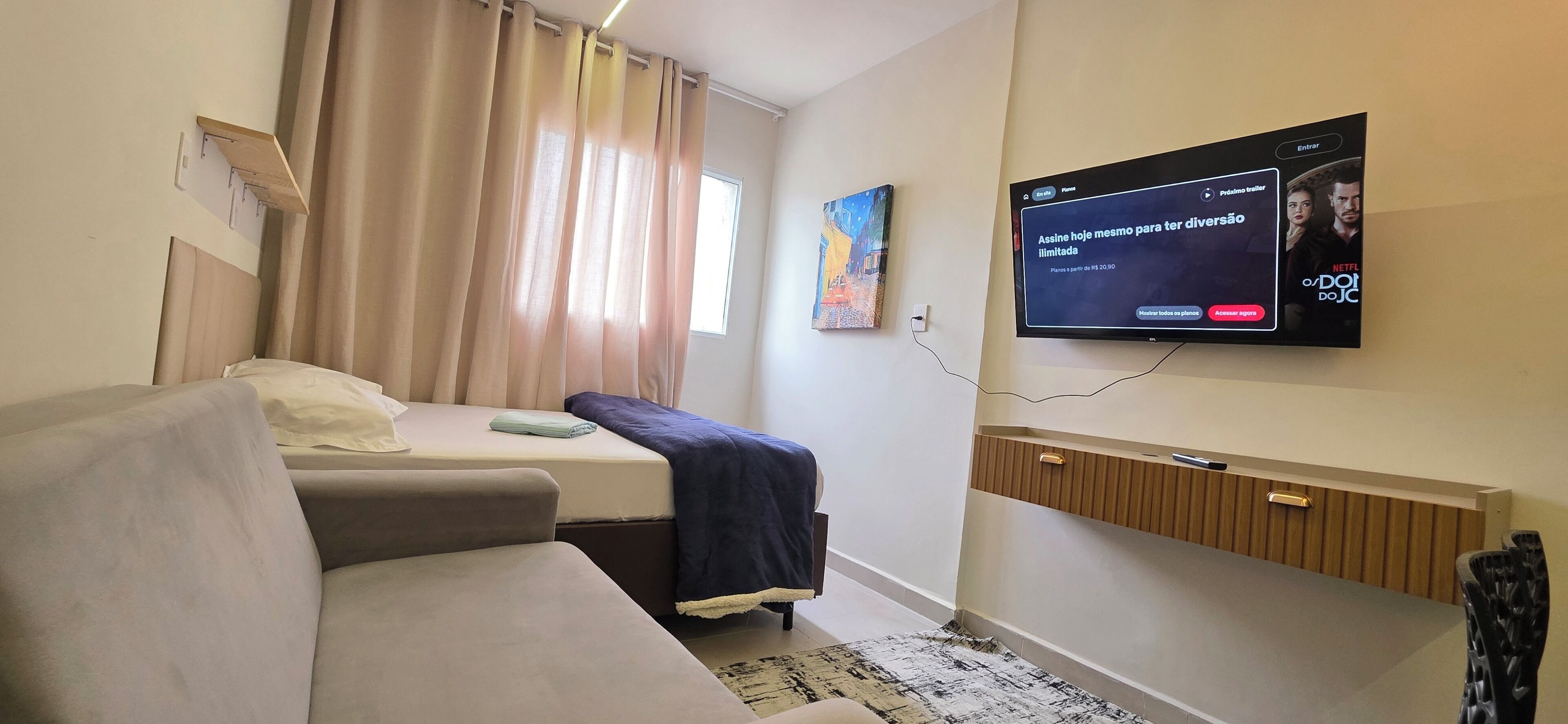 Una habitación de hotel con una cama, un sofá, un televisor montado en la pared y un cuadro.