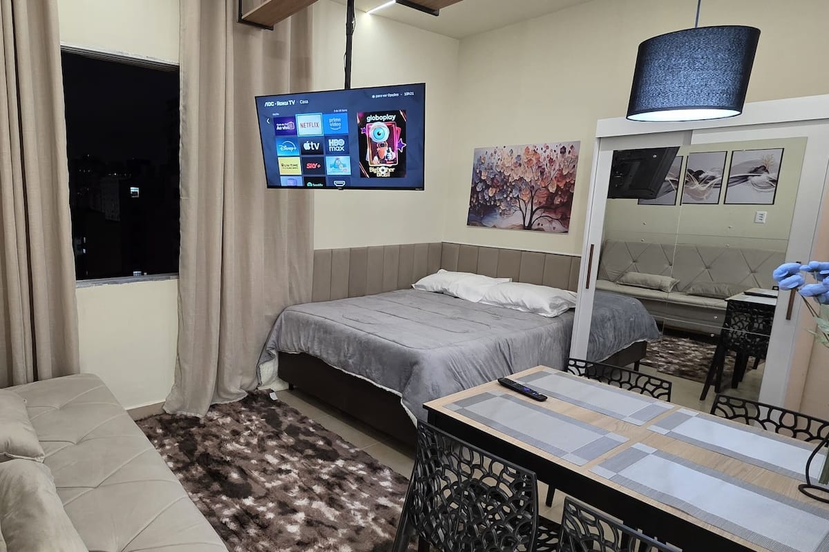 Une chambre à coucher moderne avec un lit, un canapé, un téléviseur fixé au mur et un miroir.