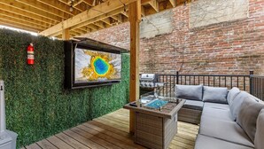 Une terrasse en bois équipée d’un téléviseur, d’un canapé d’extérieur et d’un espace barbecue.