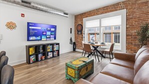 Un salon moderne avec un mur en briques, un téléviseur à écran plat, un jeu de fléchettes, une table basse en bois et un canapé en cuir.